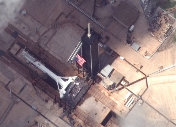 Launch pad 39A is now used by SpaceX for Falcon 9 and Falcon Heavy rocket launches. In this view captured Monday, the strongback transporter structure is seen in the horizontal position at pad 39A, with a U.S. flag waving from the fixed service structure, a tower originally built for the space shuttle and modified for SpaceX's use. Credit: Maxar Technologies