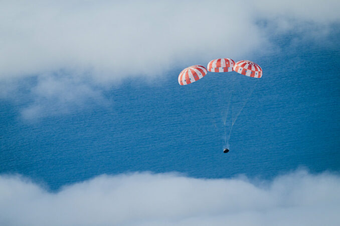 NASA's Orion spacecraft descends under three. orange and white main parachutes. Credit: NASA